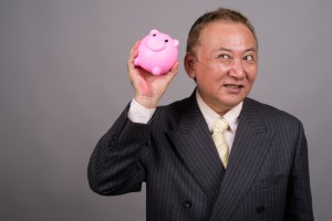 Studio Shot Of Mature Asian Businessman Holding Piggy Bank Against Gray Background Studio Shot Of Mature Asian Businessman Holding Piggy Bank Against Gray Background