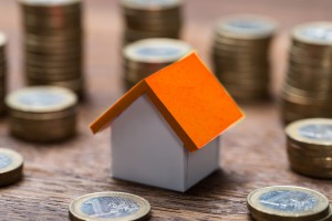 House Model Amidst Coins At Table